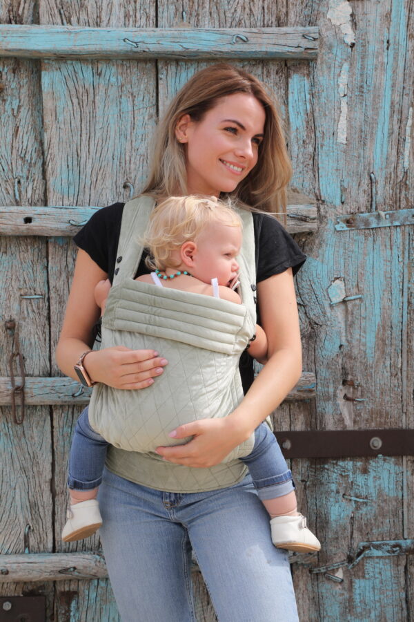 Mother carries baby daughter in light green velvet baby carrier with checked pattern