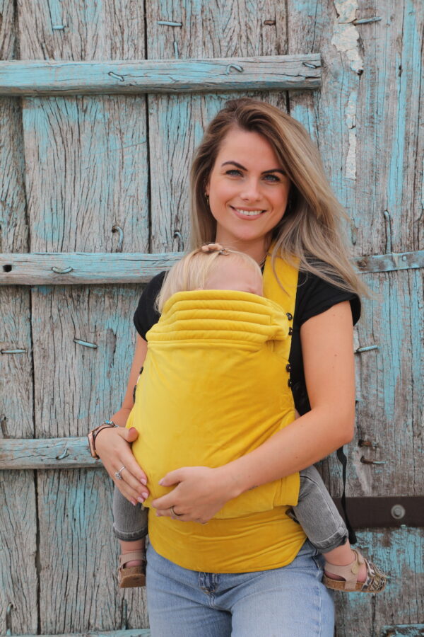 Mother carrying baby in ocher yellow velvet baby carrie on the front