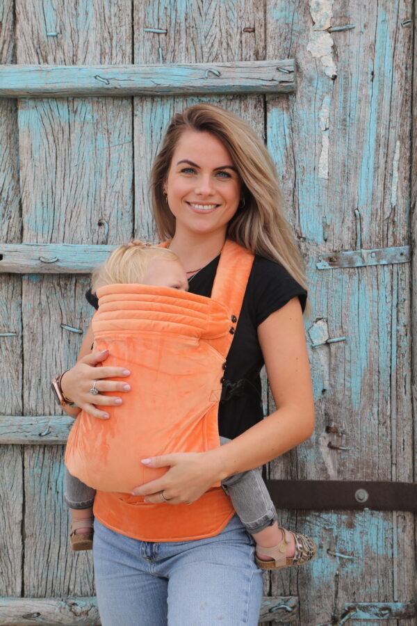 Mother carrying baby in Tangerine velvet baby carrier with adjustable straps and reversible headrest