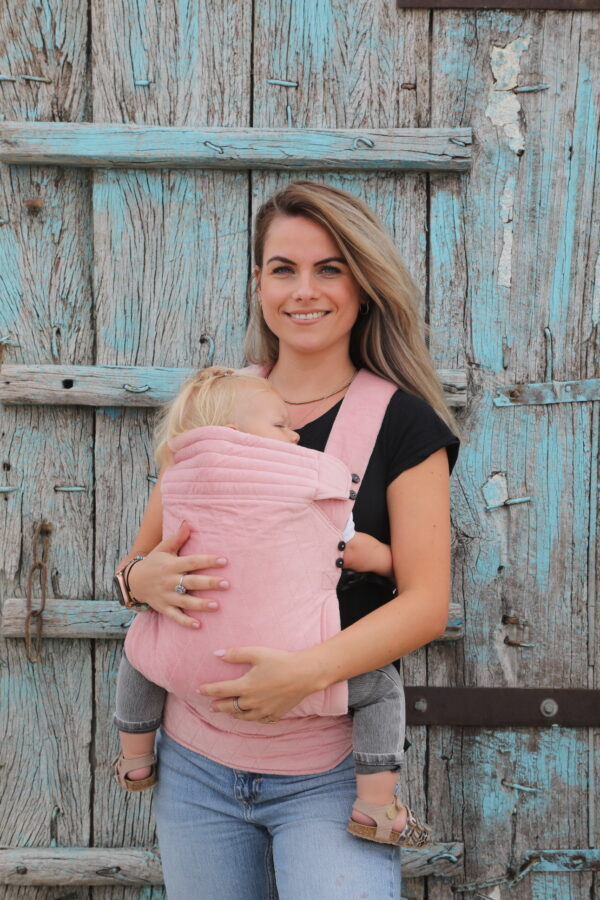 Mother carries baby in velvet soft pink baby carrier with checkered motif on the front