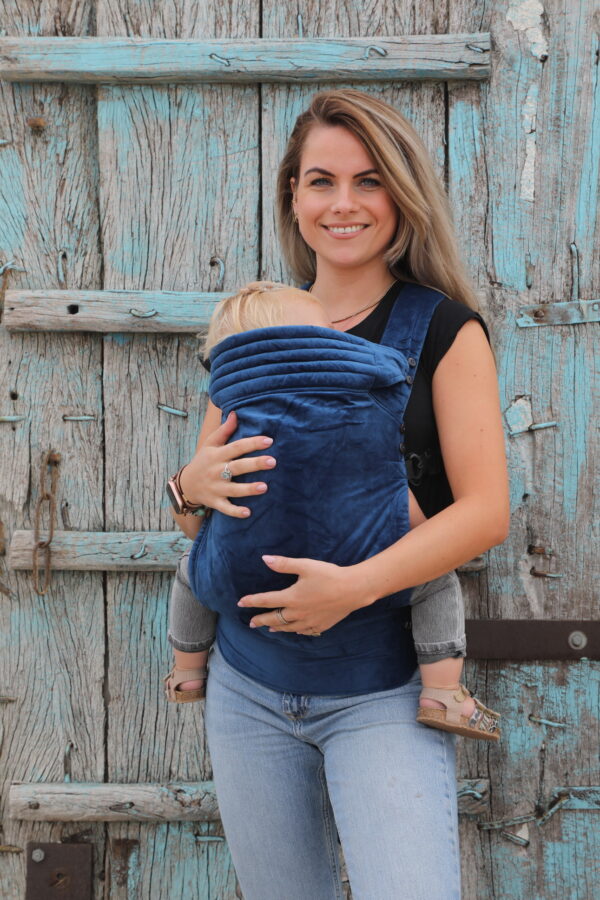 Mother carrying baby in velvet dark blue baby carrier on the front of her body