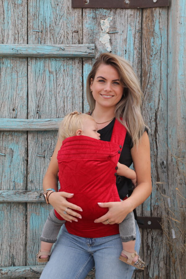 Mother carrying baby in velvet red baby carrier on the front