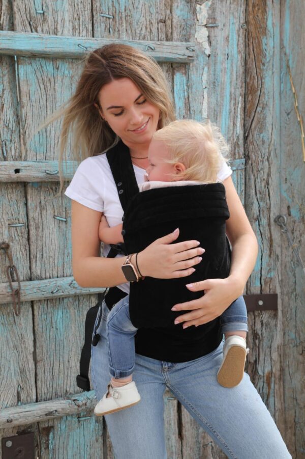 Mother carrier baby daughter in a black velvet baby carrier on the front in front of a porch